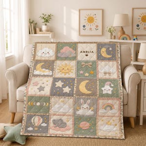 May include: A quilted baby blanket featuring a grid of squares with embroidered motifs including a smiling sun, moon, stars, clouds, a rabbit, an elephant, a rainbow, and a hot air balloon. The centre square displays the name AMELIA in dark text.