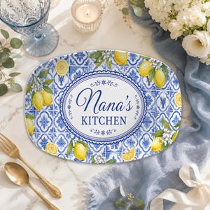 Könnte beinhalten: Eine ovale Servierplatte mit einem blau-weißen Fliesenmuster, gelben Zitronenillustrationen und grünen Blättern. In der Mitte befindet sich ein weißer ovaler Rahmen mit dem blauen Schriftzug Nana's KITCHEN in dekorativer Schrift.