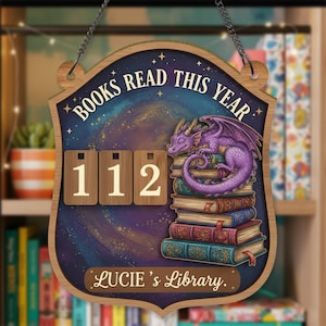 May include: Wooden sign with the text "BOOKS READ THIS YEAR" and "112". A purple dragon rests on a stack of books. The sign also says "Lucie's Library". The sign is hanging from a chain.