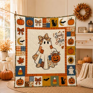 Könnte beinhalten: Eine gesteppte Tagesdecke mit einem zentralen Geistermotiv, das eine Schleife trägt und einen Kürbiseimer hält, inklusive des Schriftzugs Spooky Season. Der Rand besteht aus Patchwork-Quadraten mit Kürbissen, schwarzen Katzen, Fledermäusen und Herbstblättern.