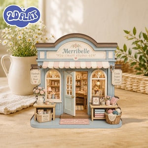 以下が含まれることがあります： Merribelle Craft Studioという名前のミニチュアクラフトスタジオモデル。水色のファサード、ストライプのオーニング、開いたドアが特徴です。店舗の両サイドには「Handmade with Heart」と「Create Inspire Dream」と書かれた看板があり、内部には棚、テーブル、ミニチュアのクラフト用品やフラワーアレンジメントが入ったバスケットが配置されています。