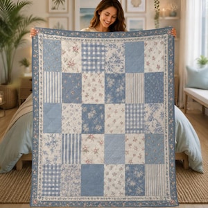 May include: A rectangular quilt featuring a patchwork design of blue and white fabric squares. The pattern alternates between floral prints, vertical stripes, and gingham checks. A decorative floral border frames the entire quilt.