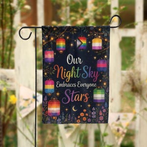 Peut inclure: Un drapeau de jardin avec un fond bleu foncé présente des lanternes colorées et le texte "Our Night Sky Embraces Everyone Stars". Les lanternes affichent des motifs arc-en-ciel et des drapeaux de la fierté LGBTQ+. Le drapeau est suspendu à un support en métal noir.