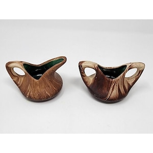 May include: Two ceramic, brown and cream-colored, small bowls with a unique design. Each bowl has a handle and a dark green interior. The exterior has a textured, wood-grain appearance. The bowls are set against a white background.