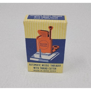 May include: A vintage box for an automatic needle threader with thread cutter. The box is yellow with blue panels and features an orange illustration of the tool. Text on the box reads "Automatic Needle Threader With Thread Cutter Made in Hong Kong."