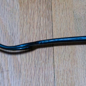 May include: A dark blue metal pry bar with a curved, pointed end. The tool is lying on a wooden surface. The pry bar is designed for leverage and prying objects apart.