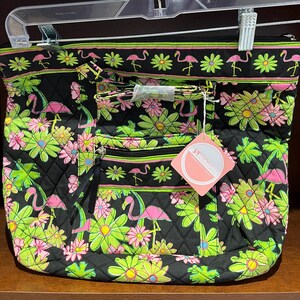 May include: Black quilted tote bag with a vibrant floral and flamingo pattern. The design features pink flamingos, green daisies, and pink flowers against a black background. The bag has a zipper closure, a tassel, and a tag.