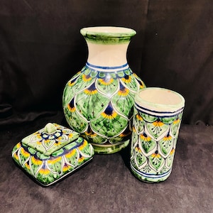 May include: A set of three hand-painted ceramic pieces: a vase, a cylindrical container, and a square lidded box. The pieces feature a green, yellow, and blue feather-like pattern on a white background. The vase is approximately 25 cm tall.
