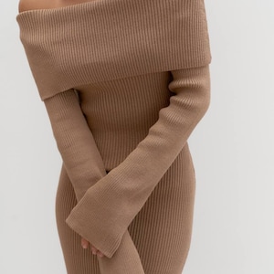 Könnte beinhalten: Ein beigefarbenes schulterfreies Kleid mit langen Ärmeln. Das Kleid ist aus einem Rippstrickstoff gefertigt und hat eine figurbetonte Silhouette. Die Ärmel sind lang und am Handgelenk ausgestellt. Das Kleid hat eine neutrale Farbe und scheint eine Midi-Länge zu haben.