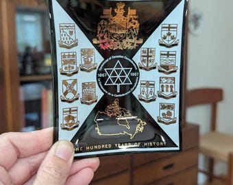 May include: Black and gold square glass dish commemorating the Centennial of Canadian Confederation in 1967. Features a map of Canada, coats of arms, and the text "ONE HUNDRED YEARS OF HISTORY."