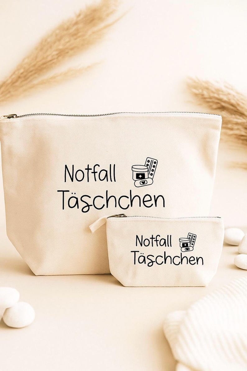 May include: Two beige canvas cosmetic bags with black text and illustrations. The larger bag has a zipper closure and the words "Notfall T&auml;schchen" and a pill bottle and pills illustration. The smaller bag has the same text and illustration.