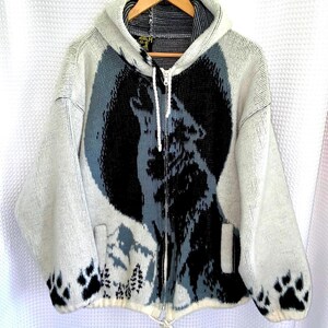 Peut inclure: Un sweat à capuche zippé en tricot gris clair avec un grand motif de loup hurlant devant une lune sombre. Le design présente des silhouettes de montagnes et des pins en bas, avec des empreintes de pattes noires sur les poignets et un cordon blanc.