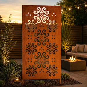 May include: A large, rectangular, rusty-orange metal privacy screen with intricate cut-out floral and scroll designs. The screen stands on two legs and is illuminated by the warm glow of a sunset and outdoor lighting. The screen is a decorative garden element.