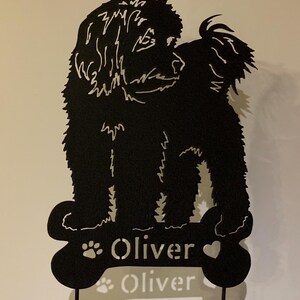 May include: Black metal silhouette of a dog standing on a bone-shaped base with the name "Oliver" written on it.