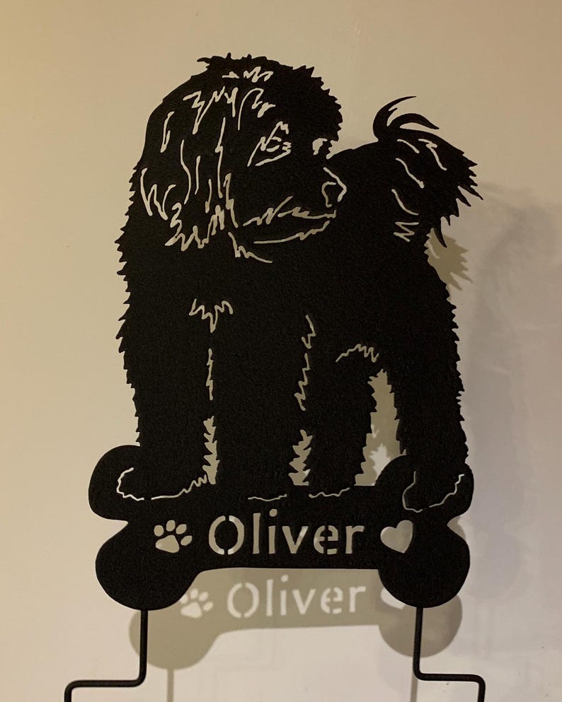 May include: Black metal silhouette of a dog standing on a bone-shaped base with the name "Oliver" written on it.