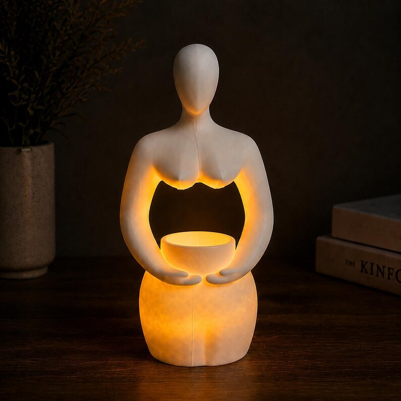 Op de afbeelding: Een witte, abstracte sculptuur van een vrouwelijke vorm die een gloeiende, ronde lichtbron vasthoudt. De sculptuur heeft een minimalistisch ontwerp met zachte rondingen en een zacht, warm licht dat van binnenuit komt. Geplaatst op een donker houten oppervlak.
