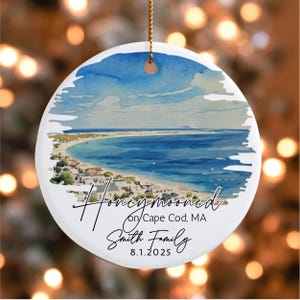 May include: Round ceramic ornament with a watercolor painting of a beach scene, blue sky, and ocean. Text reads "Honeymooned on Cape Cod, MA Smith Family 8.1.2025". The ornament has a gold string for hanging.