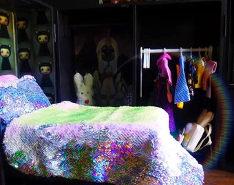 Könnte beinhalten: Ein Puppenhaus-Schlafzimmer mit einem Bett mit Paillettenüberzug, einem weißen Stoffhasen und einem Kleiderschrank mit Kleidern an einer Kleiderstange.