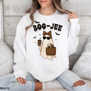 Może przedstawiać: Biała bluza z napisem "BOO-JEE" nad kresk&oacute;wkowym duchem w okularach przeciwsłonecznych, kokardą w panterkę i trzymającym kubek z kawą i torbę w panterkę. W projekcie znajdują się r&oacute;wnież czarne nietoperze i gwiazdy.