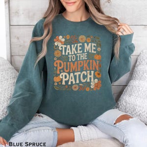May include: Blue spruce sweatshirt with the text "TAKE ME TO THE PUMPKIN PATCH" in orange and white. The design includes floral and pumpkin graphics. The sweatshirt is a crew neck style.