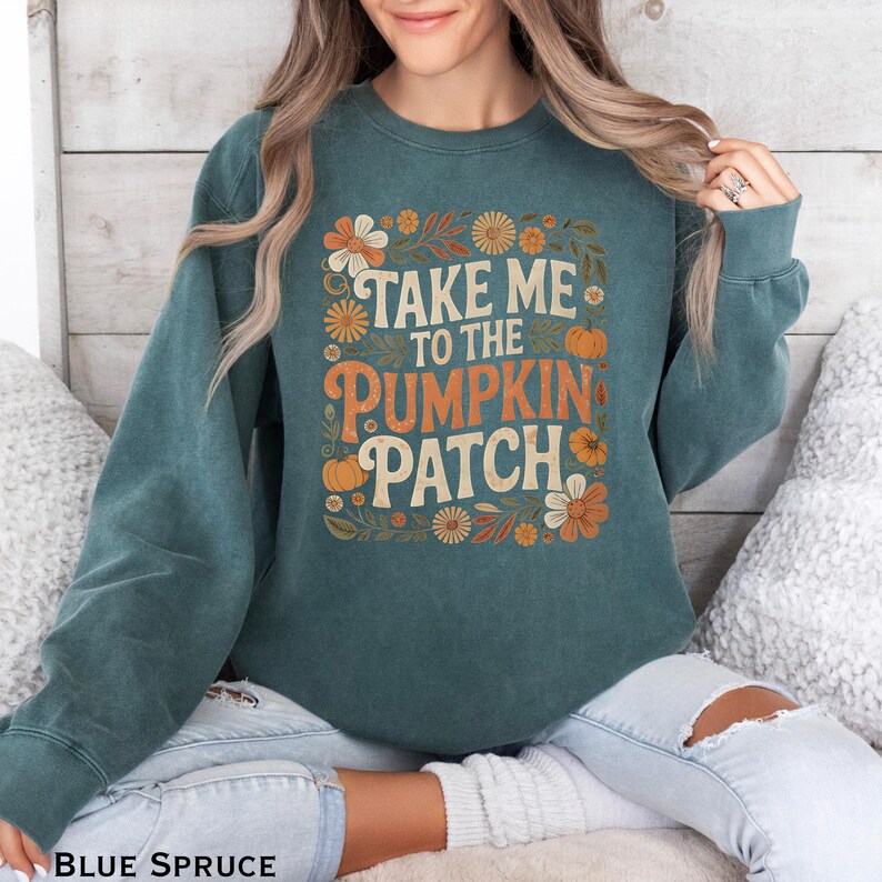 May include: Blue spruce sweatshirt with the text "TAKE ME TO THE PUMPKIN PATCH" in orange and white. The design includes floral and pumpkin graphics. The sweatshirt is a crew neck style.
