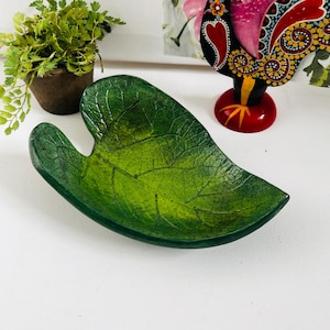 Peut inclure: Un plat décoratif vert en forme de feuille avec des nervures détaillées. Le plat a une finition brillante et est posé sur une surface blanche. C'est un objet décoratif pour la maison.