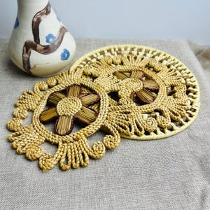 May include: Three woven straw coasters with a flower design in the centre. The coasters are beige and brown with a raised edge.