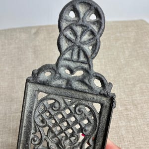May include: A black cast iron fireplace grate with an intricate design. The grate has a decorative top with a circular pattern and a lower section with a lattice design.