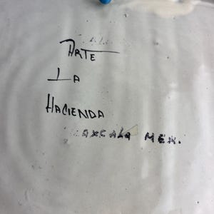 May include: White ceramic plate with black handwritten text. The text reads "Arte La Hacienda Oaxaca Mex."