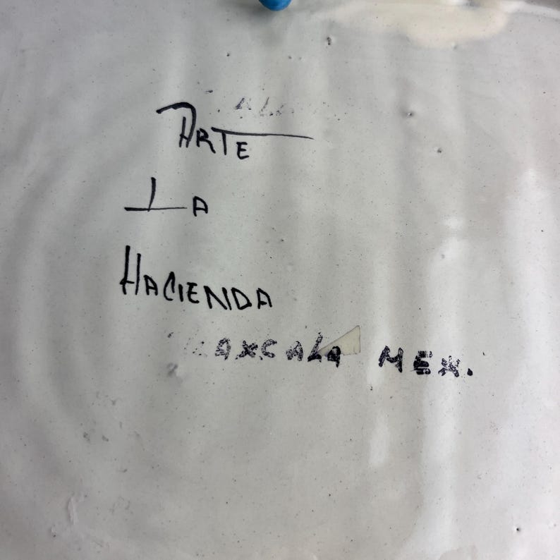 May include: White ceramic plate with black handwritten text. The text reads "Arte La Hacienda Oaxaca Mex."