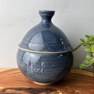 May include: A set of three ceramic mugs with a speckled, matte finish in cream, light grey, and dark grey. Each mug has a simple, minimalist design and a rounded handle.