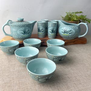 May include: A light blue tea set featuring a teapot, creamer, cups, and bowls, all with a floral pattern. The set is arranged on a wooden board. The tea set is displayed on a neutral-colored surface.