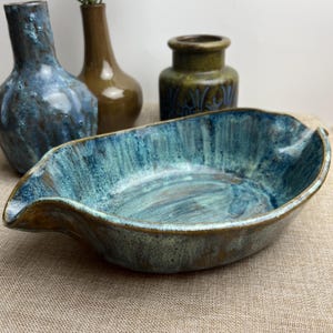 May include: A blue and brown ceramic serving dish with a wavy edge. The dish is oval shaped and has a glazed finish.