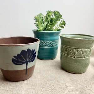 May include: Three ceramic planters, one with a blue flower design, one with a teal glaze and geometric pattern, and one with a green glaze and geometric pattern.