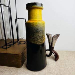 May include: A striking ceramic vase with a colour gradient. The top is yellow, transitioning to a speckled brown, and then a deep black at the base. A smaller, brown, decorative object is next to the vase.