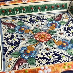 May include: Square ceramic serving dish with a hand-painted floral design. The dish features a cream-colored background with blue, red, orange, and green flowers and leaves. The rim has a green and red border, and the overall style is reminiscent of traditional Mexican pottery.
