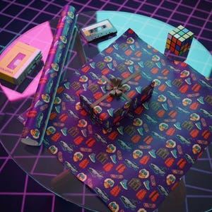 May include: A wrapped gift and roll of wrapping paper with a repeating pattern of objects on a purple background. A brown ribbon adorns the gift. A cassette tape, a Rubik's Cube, and a yellow cassette player are also visible on a glass table.