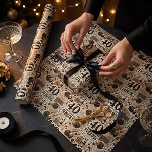 Peut inclure: Papier cadeau avec l'inscription "40 and Fabulous" et des accents dorés. Une personne noue un ruban noir sur un cadeau emballé. On aperçoit également des ciseaux dorés et un rouleau de papier.