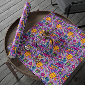 May include: A roll of Y2K-themed wrapping paper and a wrapped gift box with a brown ribbon sit on a wooden table. The paper features a repeating pattern of retro game consoles, candy canes, and the text "Y2K XMAS" and "Dunkaroos" in a vibrant color palette.
