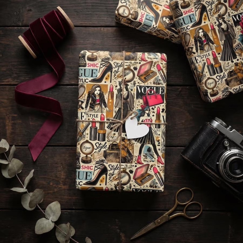 May include: Gift-wrapped packages with fashion-themed paper featuring illustrations of high heels, lipstick, and the word "Vogue." A spool of burgundy velvet ribbon, a vintage camera, and scissors are arranged on a dark wooden surface.