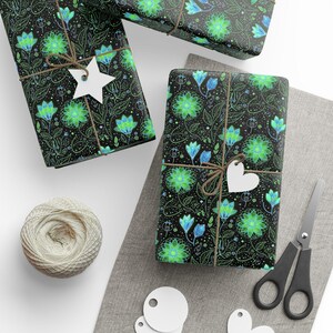 May include: Gift-wrapped presents with a black floral pattern featuring green and blue flowers. Each package is tied with twine and a white tag. A ball of twine, scissors, and blank tags are also visible.