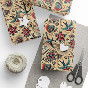 Może przedstawiać: Prezenty zapakowane w papier z motywem tatuażu w stylu vintage. Papier do pakowania zawiera kotwice, róże, jaskółki, serca i gwiazdy w kolorze czerwonym, niebieskim i beżowym. Sznurek i białe zawieszki w kształcie serca służą do zabezpieczenia prezentów.