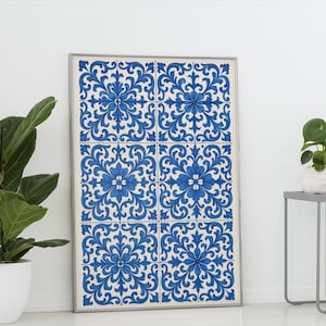 May include: A framed artwork featuring a repeating pattern of blue floral designs on a white background. The artwork is displayed against a white wall, with a potted plant on the left and a small table with a plant on the right.
