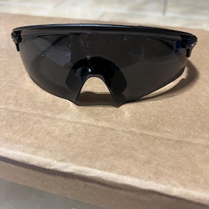 Puede incluir: Gafas de sol deportivas negras con un diseño envolvente. Las gafas de sol tienen lentes oscuras y tintadas y una montura elegante y moderna. El puente de las gafas tiene una forma curva única.
