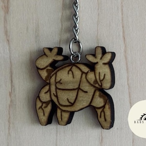 May include: A wooden keychain featuring a stylized crab design. The crab is light brown with darker brown etched details and a silver chain. The keychain has a unique, handcrafted appearance, perfect for ocean lovers.