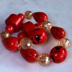 May include: A bracelet with red and gold beads. The red beads are in different shapes, including round, oval, and cylindrical. Some red beads have black spots. The gold beads are faceted, adding a sparkling effect.