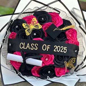 May include: A bouquet of black and pink silk roses with a gold butterfly, a graduation cap, and a black ribbon with the text "CLASS OF 2025".
