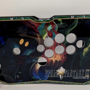 May include: A rectangular arcade controller featuring a Final Fantasy IX graphic with a character holding a flame. The device has eight white circular buttons arranged in a curved layout on the surface and a gold-colored border trim.