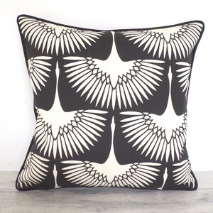 May include: Square decorative pillow with a black background and a repeating white crane design. The pillow has a black border and is placed against a white background.
