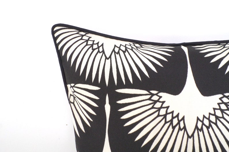 May include: Close-up of a black and white decorative pillow. The pillow features a repeating pattern of stylized white birds against a black background. The pillow has a black border.